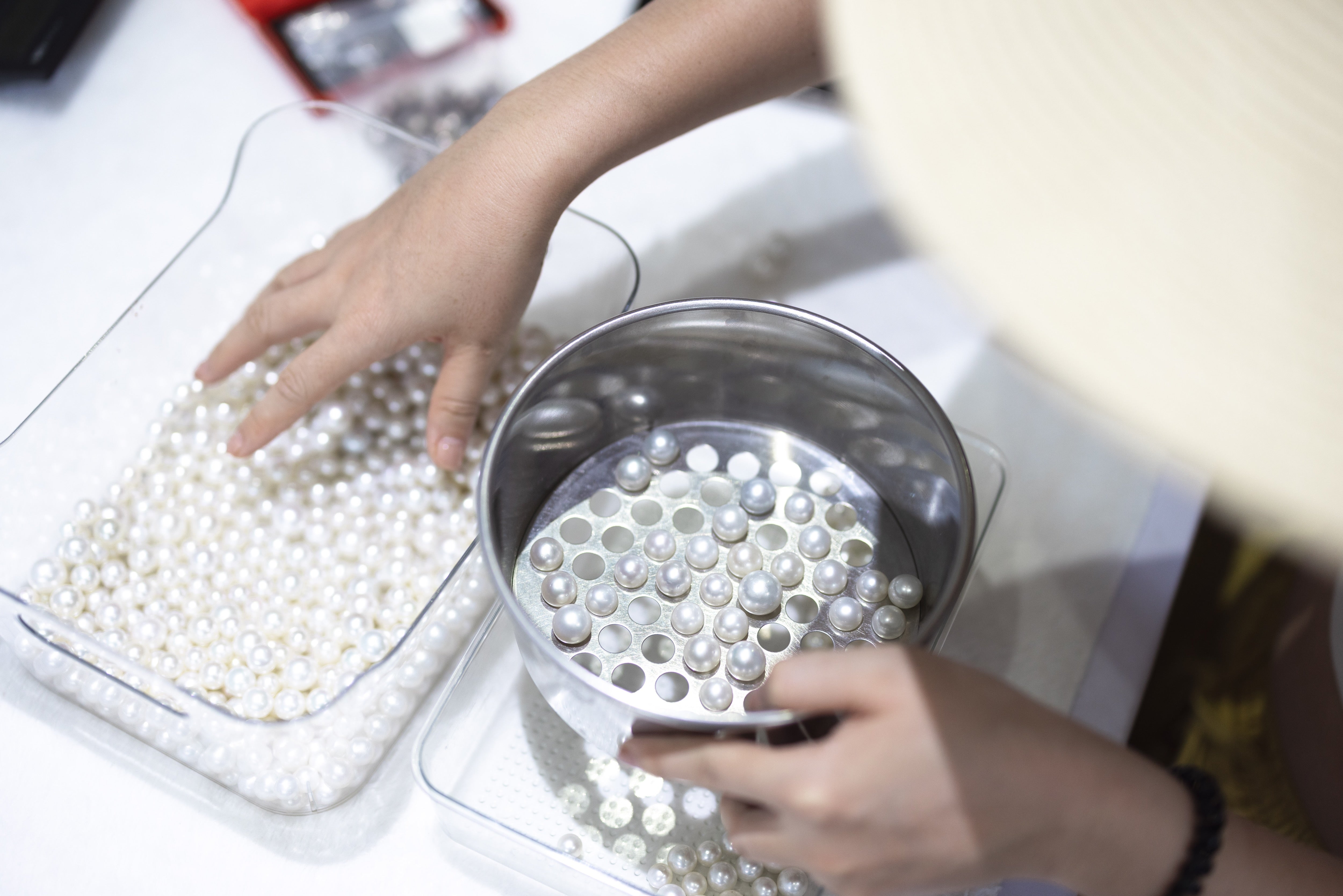 Person sorting pearls into a container on a white surface