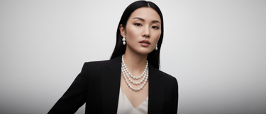 Woman wearing a black blazer and pearl necklace against a gray background